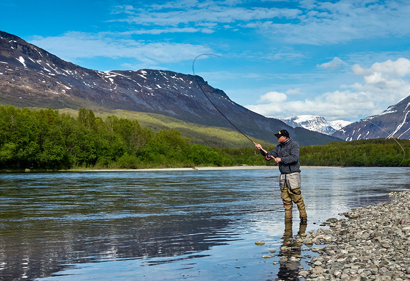 A man fly fishing in a river against the background of mountains.